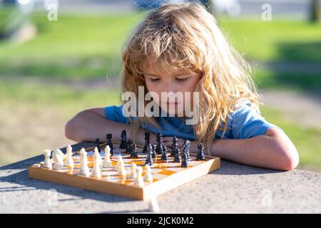 Enfant élève pensant à sa prochaine étape dans une partie d'échecs. Petit garçon concentré assis à la table et jouant aux échecs. Banque D'Images