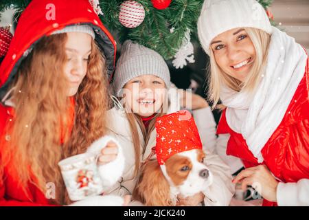 Une mère célibataire avec deux enfants et un chien s'amusent dans le coffre de voiture avec une décoration de Noël rouge, bonne boisson familiale chocolat chaud de la tasse. Vacances d'hiver Banque D'Images