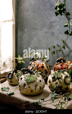 Décorations d'Halloween, ensemble de citrouilles en céramique sculptées blanches et brunes sur une table avec des feuilles de lierre près de la fenêtre. Fête d'Halloween int Banque D'Images