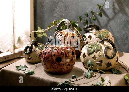 Décorations d'Halloween, ensemble de citrouilles en céramique sculptées blanches et brunes sur une table avec des feuilles de lierre près de la fenêtre. Fête d'Halloween int Banque D'Images