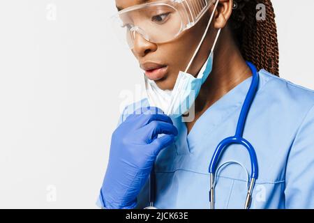 Femme enceinte noire médecin portant un masque facial posant avec un stéthoscope isolé sur fond blanc Banque D'Images