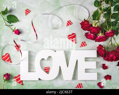 Composition festive de l'amour pour la Saint-Valentin faite avec des roses rouges, des coeurs et du mot Amour. Pose à plat. Banque D'Images