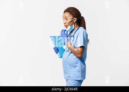 Femme enceinte noire médecin portant un masque facial posant avec un stéthoscope isolé sur fond blanc Banque D'Images
