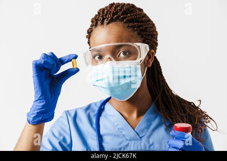 Médecin enceinte noire portant un masque facial montrant la pilule isolée sur fond blanc Banque D'Images