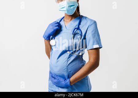 Femme enceinte noire médecin portant un masque facial posant avec un stéthoscope isolé sur fond blanc Banque D'Images
