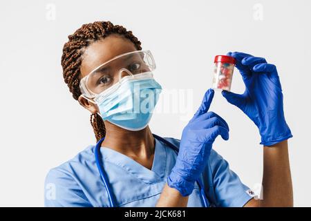 Médecin enceinte noire portant un masque facial montrant des pilules isolées sur fond blanc Banque D'Images