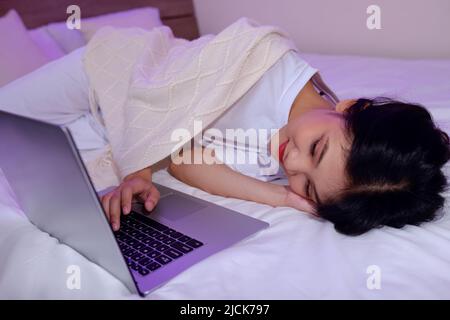 Fille endormi sur un lit sous une couverture et regardant un film sur un ordinateur portable ou un ami qui appelle des vidéos Banque D'Images