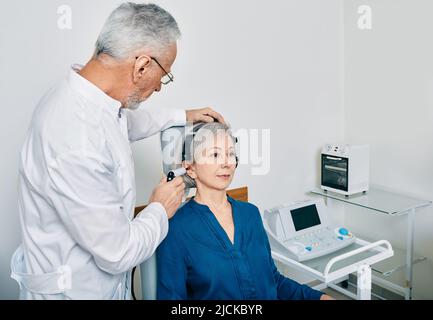 Audiologiste mature avec sonde de tympanomètre faisant la procédure tympanométrie ou audiométrie d'impédance pour la patiente sénior à la clinique d'audition Banque D'Images