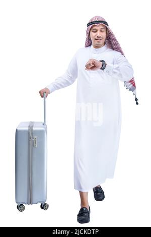 Homme arabe portant du keffiyeh regardant la montre à son poignet avec une valise pour voyager isolé sur fond blanc Banque D'Images