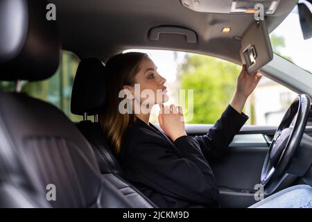 Jeune femme attirante regardant dans le miroir tout en conduisant la voiture. Banque D'Images