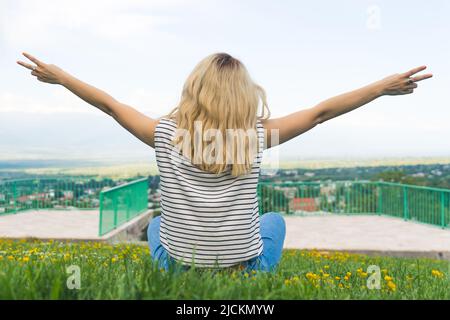 fille blonde assise sur l'herbe et tenant les mains étirées dans le parc. tir moyen extérieur. Photo de haute qualité Banque D'Images