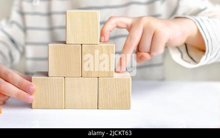 Les mains des enfants jouent et construisent un escalier à partir de cubes, les doigts grimpant l'échelle vers le haut de blocs de bois. Le concept de la victoire, la voie du succès Banque D'Images