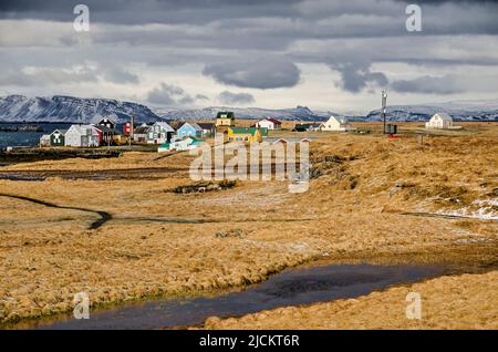 Flatey, Islande, 5 mai 2022 : vue sur les champs jaune-marron, partiellement enneigés, vers le village et le fjord et les montagnes au-delà Banque D'Images