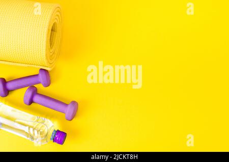 Home fitness concept jaune tapis de yoga, deux haltères violettes et une bouteille d'eau. Équipement de formation et exercices pour la perte de poids. Pose à plat. Banque D'Images