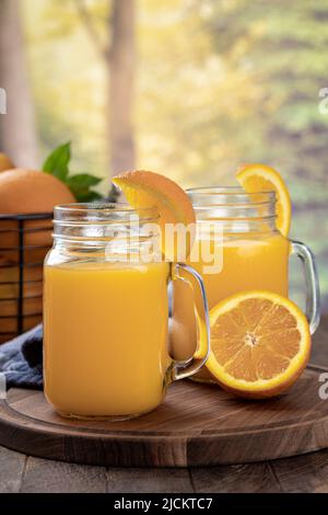 Deux verres de jus d'orange avec des lamelles d'orange sur un plateau en bois avec un fond rural d'été Banque D'Images