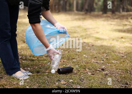 Une femme tient les mains dans des gants pour recueillir et mettre la bouteille de plastique usagée dans un sac poubelle bleu. Un volontaire nettoie le parc par une journée ensoleillée. Effacement, p Banque D'Images