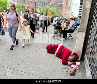 L'homme dort dans ce qui semble être une suite de Santa sur le trottoir sur 14th Street en face de Union Square que les gens passent par un chaud jour de printemps. Manhattan, New York. Banque D'Images