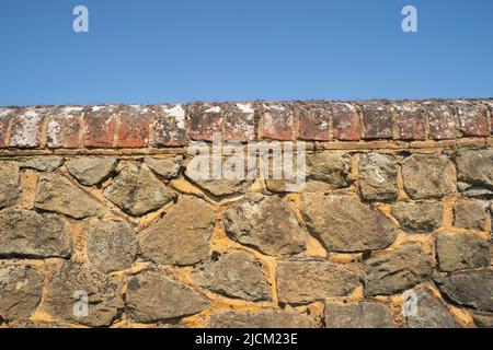 Kentish ragstone calcaire gris dur utilisé pour construire un mur frontière fort avec la brique rouge et le lichen sur le dessus contre un ciel bleu Banque D'Images