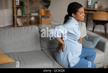 Femme noire enceinte souffrant de douleurs dans le bas du dos assise à la maison Banque D'Images