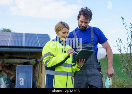 Homme et femme installateurs solaires ingénieurs avec la tablette tout en installant le système de panneau solaire à la maison. Banque D'Images