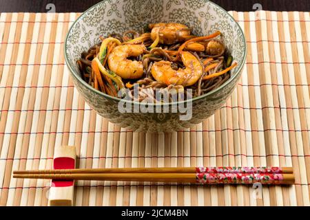 Au-dessus de l'appétissant plat traditionnel japonais de yakisoba avec crevettes et légumes frits servis sur un tapis de bambou avec des baguettes dans le restaurant Banque D'Images