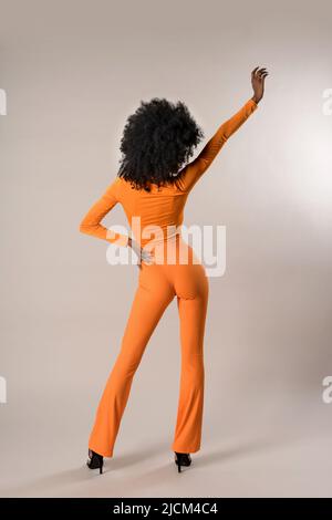 Vue arrière du corps entier d'une femme afro-américaine mince anonyme en costume serré debout sur fond blanc avec bras relevé en studio Banque D'Images
