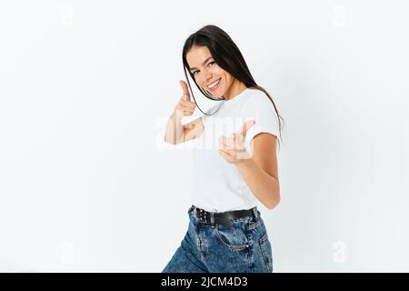 Confiante heureuse femme portant un T-shirt blanc simple et bleu jeans pointe vers l'appareil photo avec les deux mains, sympathique expression optimiste, blanc studio b Banque D'Images