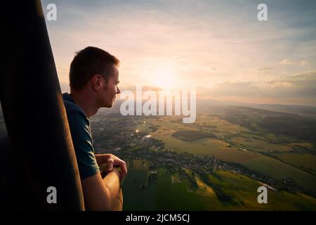 Homme profitant de la vue depuis un ballon d'air chaud pendant le vol sur un paysage magnifique au coucher du soleil. Thèmes aventure, liberté et voyage. Banque D'Images