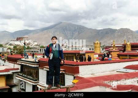 Un homme se tient sur le toit du temple de Jokhang avec le palais de Potala en arrière-plan. Banque D'Images