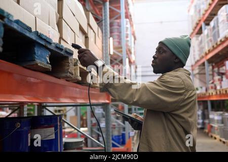 Le responsable africain scannant des paquets sur des étagères avec un dispositif spécial pendant son travail à l'entrepôt Banque D'Images