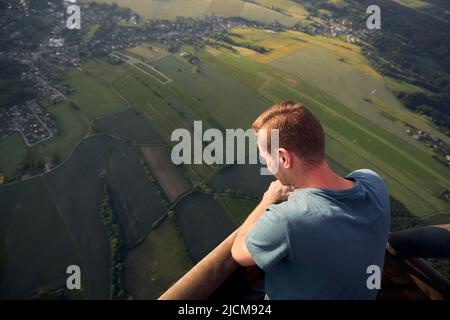 Homme profitant de la vue depuis un ballon d'air chaud pendant le vol sur un paysage magnifique au coucher du soleil. Thèmes aventure, liberté et voyage. Banque D'Images