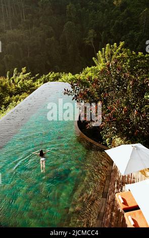 Femme nageant dans la piscine à débordement, Ubud Hanging Gardens, Bali, Indonésie. La piscine à débordement fait face à la vallée de la rivière Ayung. Banque D'Images