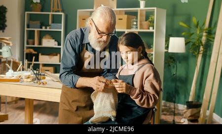 Un grand-père de Caring enseigne à sa petite-fille adolescente à coudre dans un atelier à domicile. Artisanat, Hobby. Communication des générations, Happy Family Time Banque D'Images