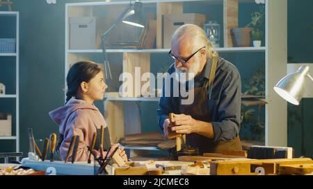 Grand-père attentionné avec sa petite-fille adolescente passer du temps ensemble, travailler sur le bois, profiter de la communication dans l'atelier. Garage passe-temps. Communicati Banque D'Images