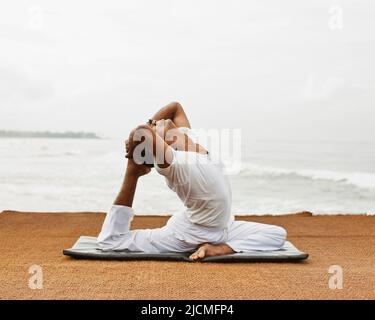 Le maître sri-lankais de yoga pratique le yoga sur la plage. Aturuwella, Bentota, Sri Lanka; on voit ici la pose de pigeon à une jambe. Banque D'Images