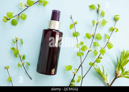 Bouteille de vaporisateur cosmétique brune et branches de bouleau avec de jeunes petites feuilles sur fond bleu. Maquette. Spray antibactérien liquide et de beauté pour les soins de la peau. NAT Banque D'Images