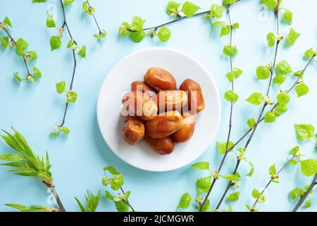 Datte les fruits dans un bol et les branches de bouleau avec de petites feuilles sur fond bleu. Vue de dessus, repose-ressort à plat Banque D'Images