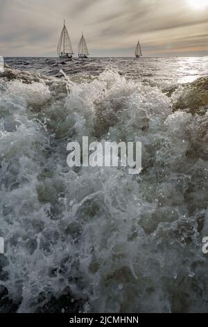 Éclaboussures d'eau de bateau à moteur en premier plan, yachts à voile au coucher du soleil en arrière-plan, régate de voile, grandes vagues Banque D'Images