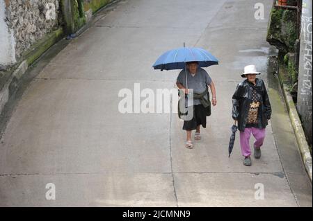 Province de montagne, Philippines : deux femmes locales, des aînés agiles tenant des parasols, descendent une route cimentée dans le centre-ville de Sagada. Banque D'Images