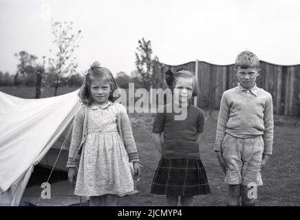 1950s, historique, trois jeunes enfants debout pour leur photo à l'extérieur d'une tente de toile de l'époque, Angleterre, Royaume-Uni. Banque D'Images