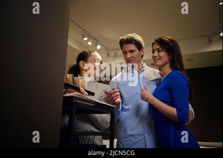 Agréable African American assistant de vente dans magasin de meubles présente aux clients divers échantillons de surfaces dures pour la rénovation de meubles de maison. Int Banque D'Images