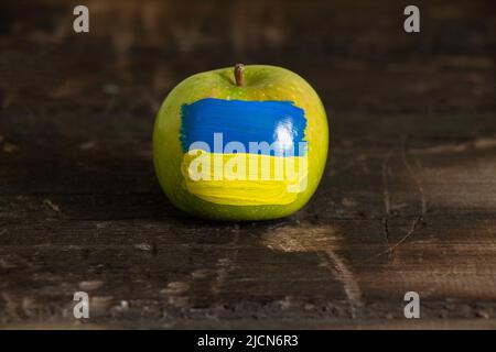 Une pomme verte avec le drapeau national de l'Ukraine en jaune et bleu se trouve sur une vieille table en bois à la maison dans la cuisine, la paix en Ukraine, la victoire Banque D'Images