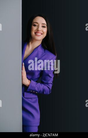 Femme charmante souriante en costume violet apparaissant à un coin de rue. Banque D'Images