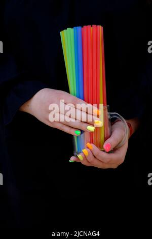 femme avec des extensions d'ongle peintes dans une variété de couleurs tenant le verre rempli de pailles de boisson en plastique coloré Banque D'Images