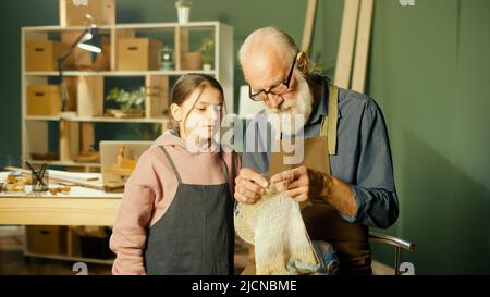 Un grand-père de Caring enseigne à sa petite-fille adolescente à coudre dans l'atelier Banque D'Images