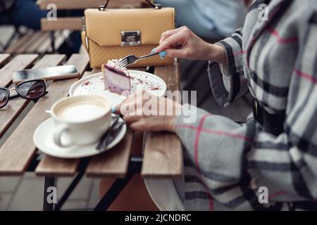 Gros plan de la femme avec une manucure bleue, avec une tarte au cheesecake et un cappuccino à la place du café. Banque D'Images