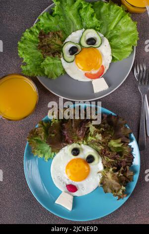 Fun Food for Kids - visages souriants à base d'œufs frits, concombres, tomates, radis, olives noires et feuilles de laitue sur deux assiettes. Créatif sain Banque D'Images