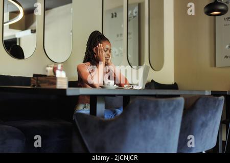 Une course mixte inquiète et fâchée femme d'affaires afro-américaine, surtravaillant en ligne avec un ordinateur portable dans un bureau créatif. Maux de tête Banque D'Images