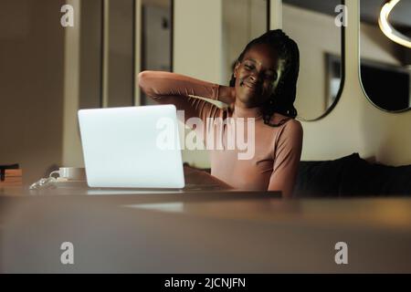 Femme d'affaires, anxieuse et fatiguée, mal de race mixte, tenir le cou, sentir la douleur, en utilisant l'ordinateur portable dans le café. Mauvaise posture, scoliose Banque D'Images
