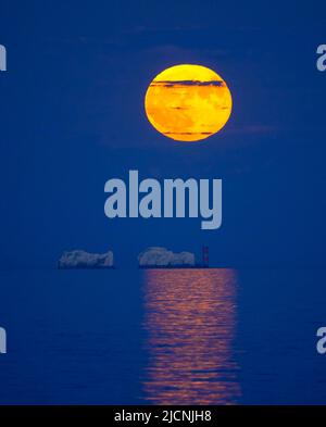 Highcliffe-on-Sea, Dorset, Royaume-Uni. 14th juin 2022. Météo Royaume-Uni. La pleine Strawberry Super Moon brille d'orange lorsqu'elle s'élève dans le ciel nocturne au-dessus du phare des aiguilles sur l'île de Wight, vue depuis Highcliffe-on-Sea à Dorset. Crédit photo : Graham Hunt/Alamy Live News Banque D'Images